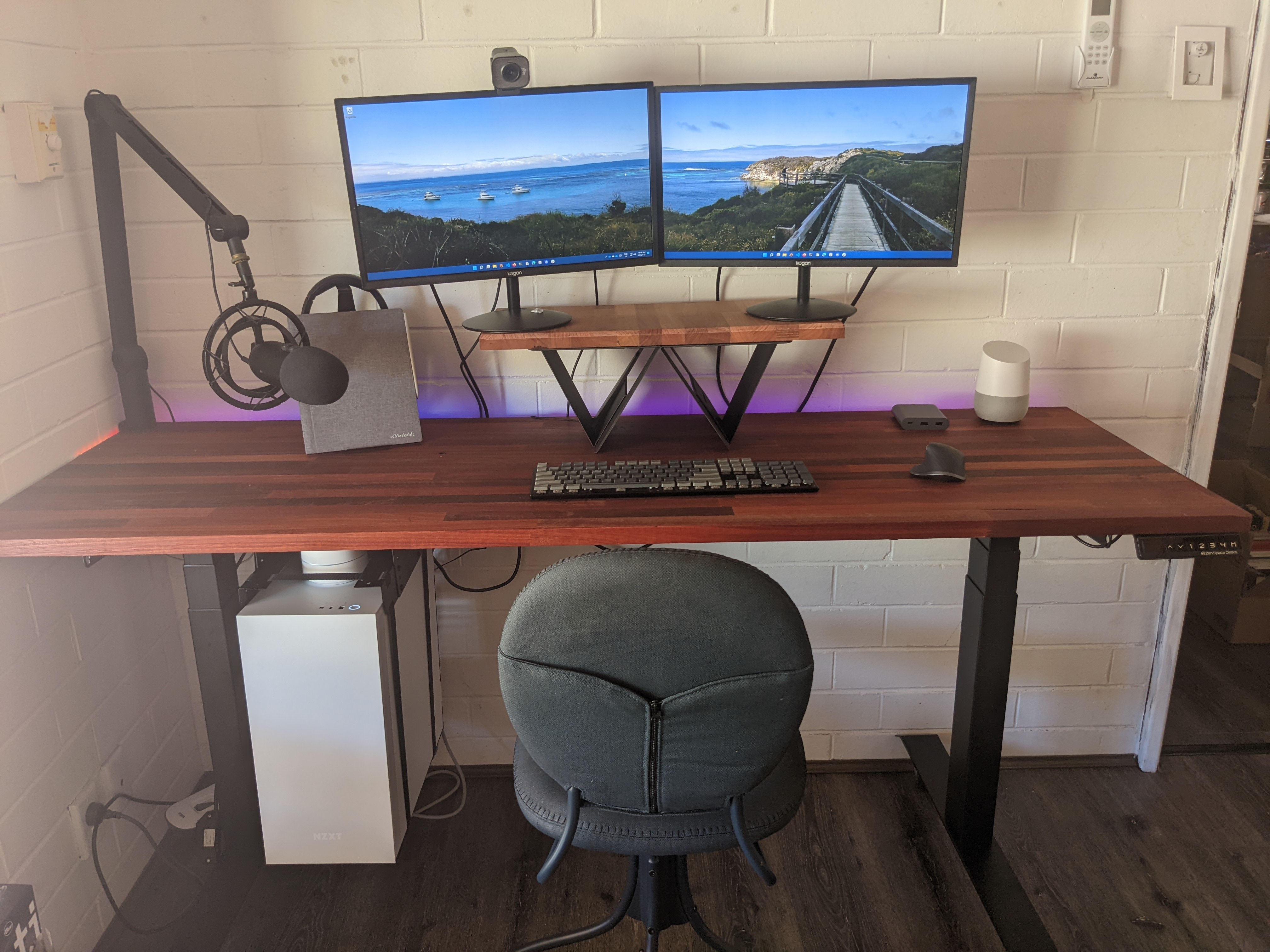Assembled desk with two monitors balanced precariously on a board on a folding laptop desk, with a mic on a boom arm swinging in from the side of the desk